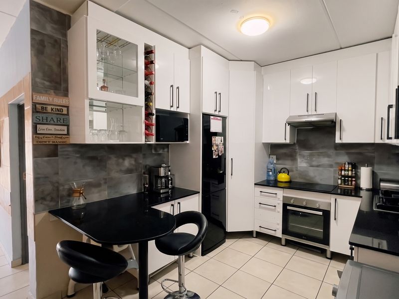 Modern kitchen featuring white cabinetry, black granite countertops, built-in oven and hob, tiled backsplash, and a convenient breakfast nook area.
