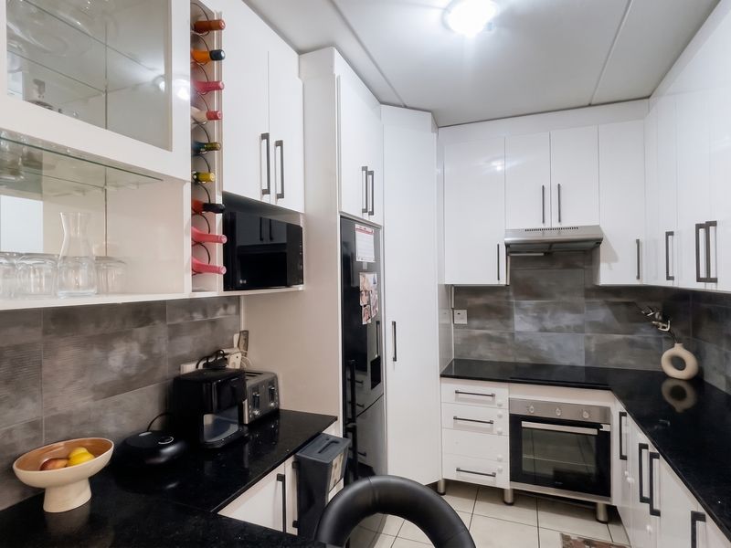 Modern kitchen featuring white cabinetry, black granite countertops, built-in oven, extractor fan, and stylish grey tiled backsplash.