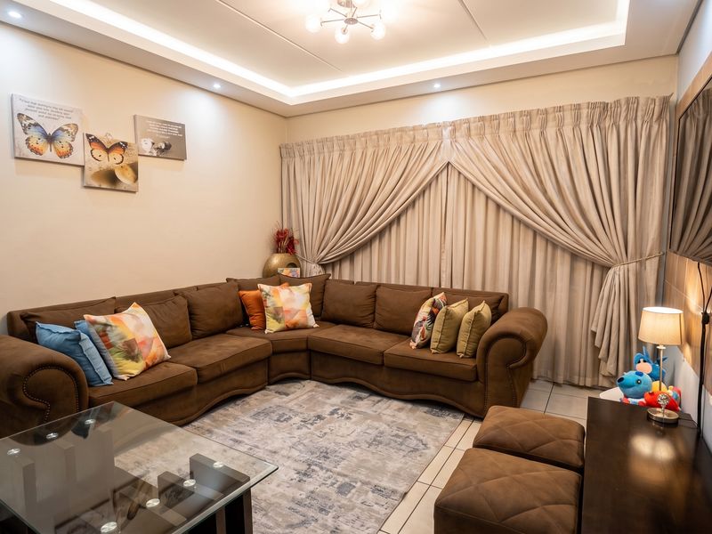 A well-maintained living room featuring recessed ceiling lighting, tiled flooring, and a tiled feature wall with a mounted television.