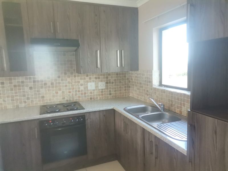 A functional kitchen featuring dark wood-look cabinetry, mosaic tile backsplash, integrated electric hob and oven, and a double bowl sink with a window.
