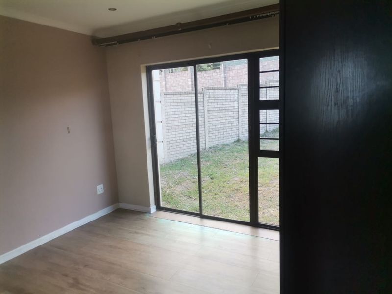 An empty living room featuring laminate flooring, recessed lighting, and a sliding glass door providing direct access to the rear garden area.