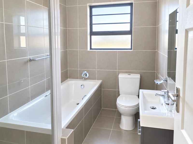 A clean, modern bathroom featuring a built-in bathtub, a vanity basin, and neutral floor-to-ceiling wall tiles.