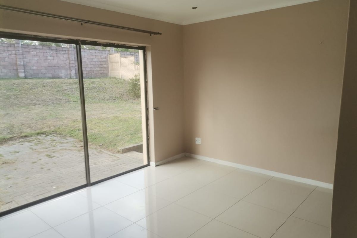 A bright, empty living room featuring large sliding glass doors that open onto a private garden area, finished with neutral tiled flooring.