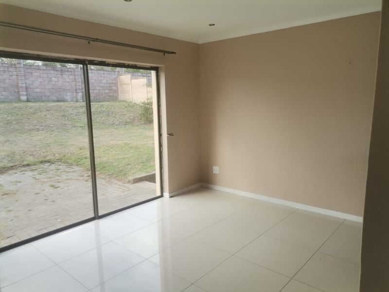 A bright, empty living room featuring large sliding glass doors that open onto a private garden area, finished with neutral tiled flooring.