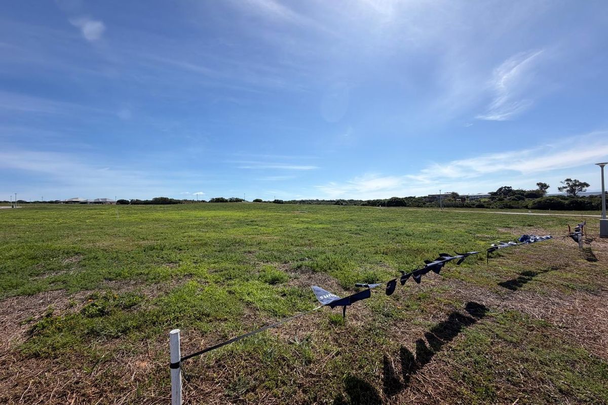 A wide-angle view of a vacant residential plot featuring open grassland and boundary markers under a clear blue sky.