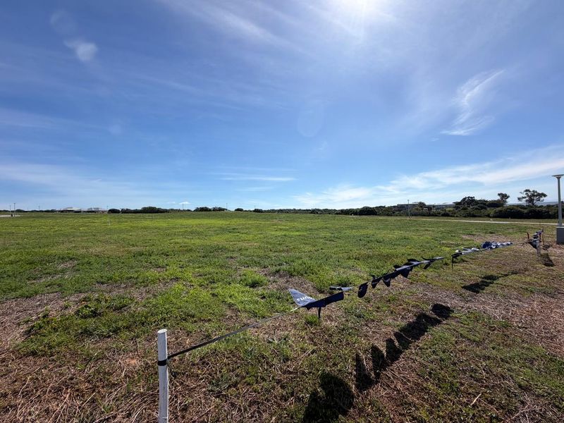 A wide-angle view of a vacant residential plot featuring open grassland and boundary markers under a clear blue sky.