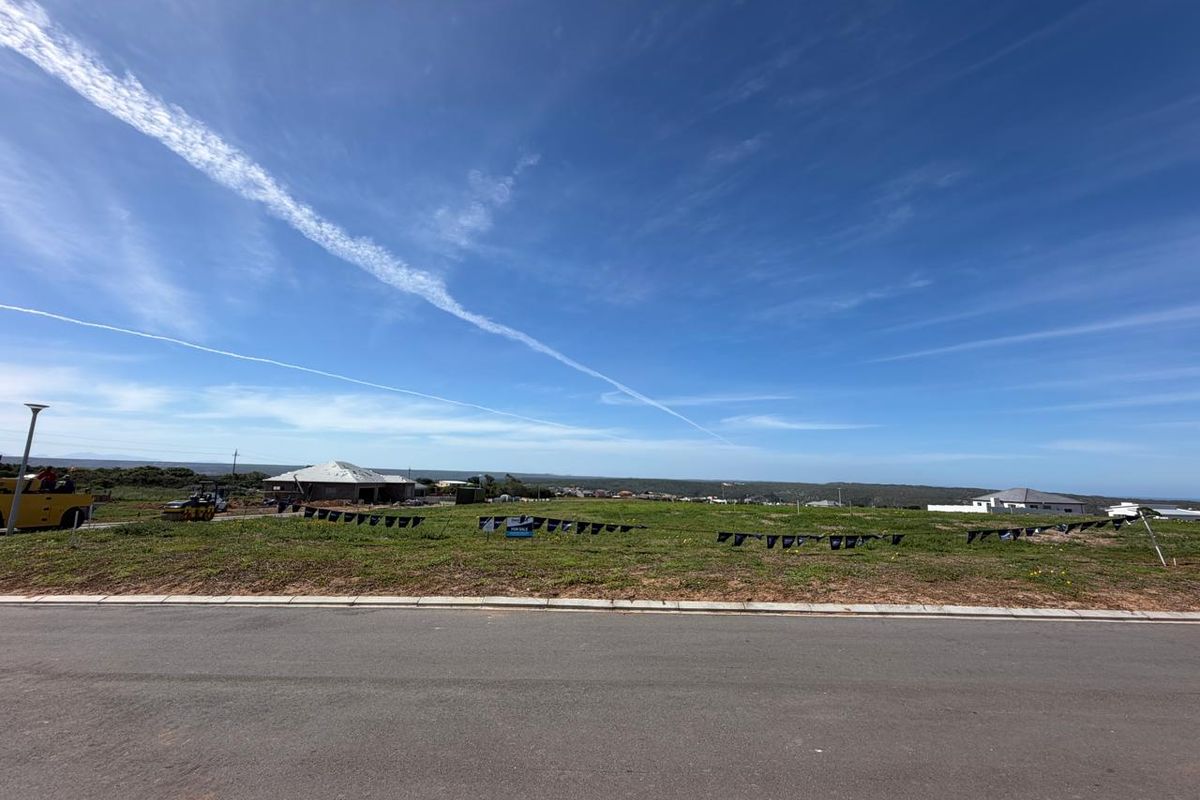 A wide-angle view of a vacant residential plot situated along a paved road, featuring open land and surrounding neighborhood development.