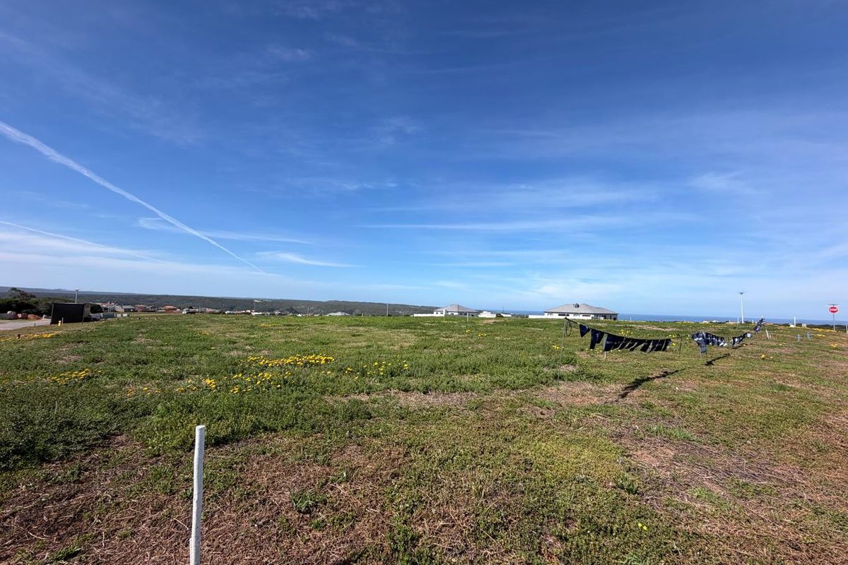 A wide-angle view of a vacant residential plot featuring open grassland and distant coastal views.