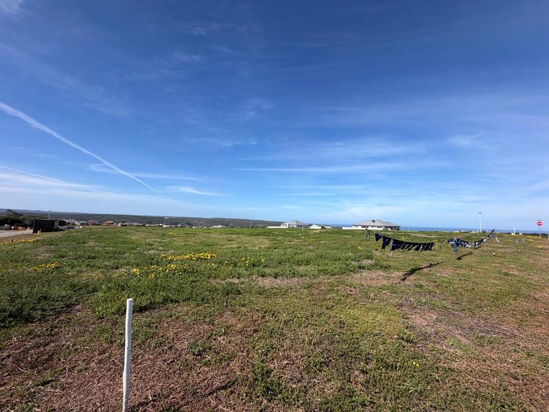 A wide-angle view of a vacant residential plot featuring open grassland and distant coastal views.
