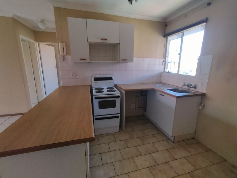 A functional kitchen featuring laminate countertops, a freestanding stove, stainless steel sink, and tiled splashback, offering a blank canvas for modern updates.