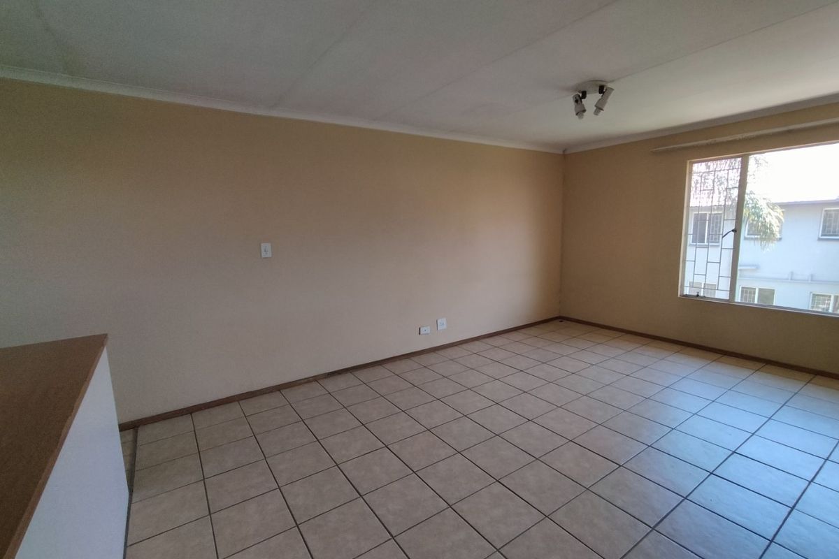 An empty, neutrally painted living area featuring tiled flooring and a window with security bars, offering a blank canvas for personalization.