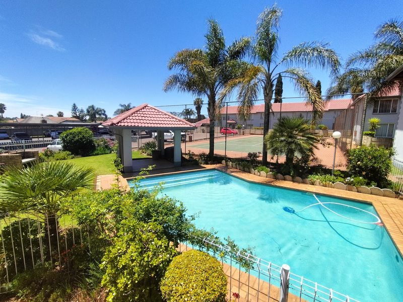Outdoor pool area featuring a gazebo, landscaped garden, and access to a communal tennis court within the townhouse complex.