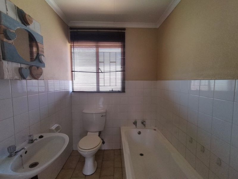 A functional bathroom featuring a standard bathtub, pedestal basin, and toilet with partial wall tiling and neutral finishes.