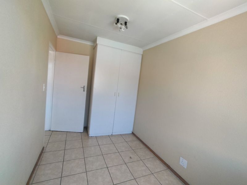 A clean, empty bedroom featuring neutral wall paint, tiled flooring, and a built-in wardrobe, offering a versatile space ready for personalization.