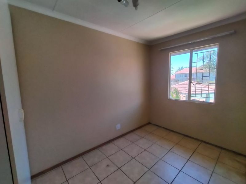 An empty bedroom featuring tiled flooring, cove cornicing, and a window fitted with security bars.
