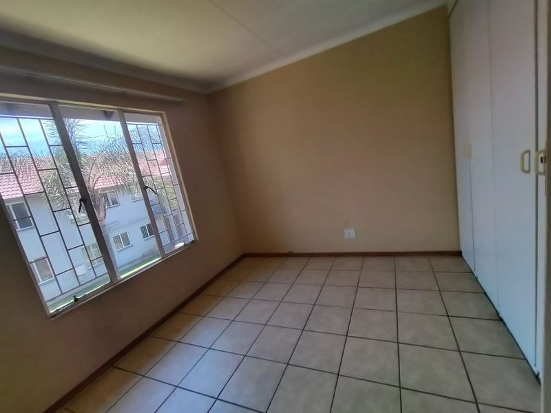 An empty bedroom featuring tiled flooring, built-in cupboards, and large windows with security bars, offering a clean and neutral space.