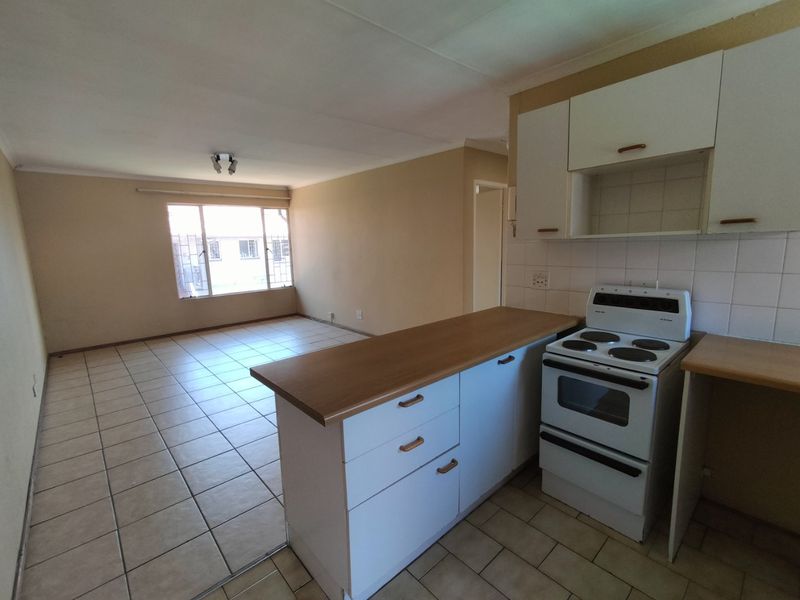 Open plan kitchen and living area featuring tiled flooring, built-in cabinetry, and a freestanding electric stove in a neutral, vacant space.