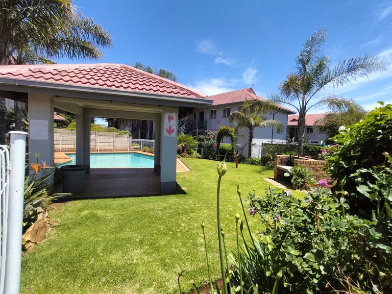 Communal outdoor area featuring a swimming pool, covered patio structure, and a brick built-in braai set within a well-maintained garden.