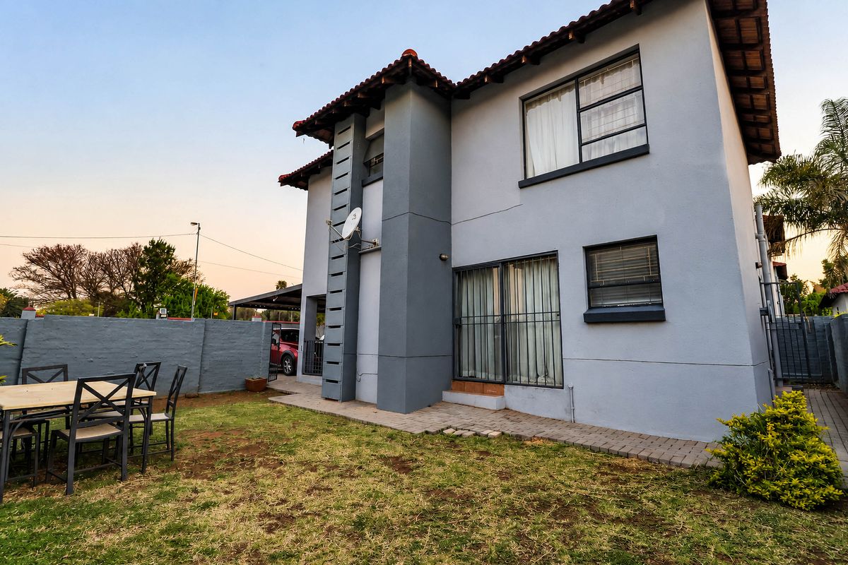 Rear view of a two-story townhouse featuring a grey facade, tiled roof, sliding glass doors with security bars, and a private garden area.