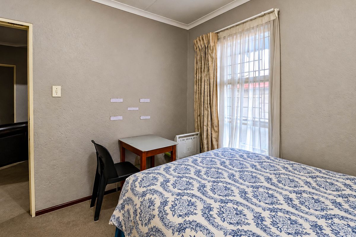 A functional bedroom featuring neutral wall finishes, carpeted flooring, and a window fitted with security bars.