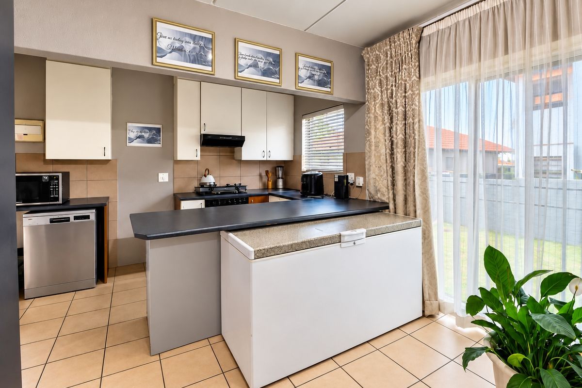 Functional kitchen featuring built-in cabinetry, gas hob, extractor fan, and tiled flooring, with direct access to the outdoor area via a sliding glass door.