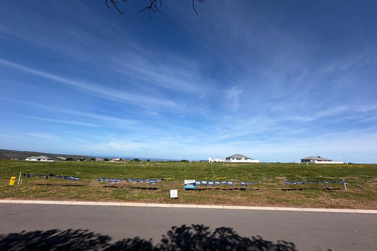 A vacant residential plot of land featuring a grassed surface, situated along a paved road with distant coastal views.