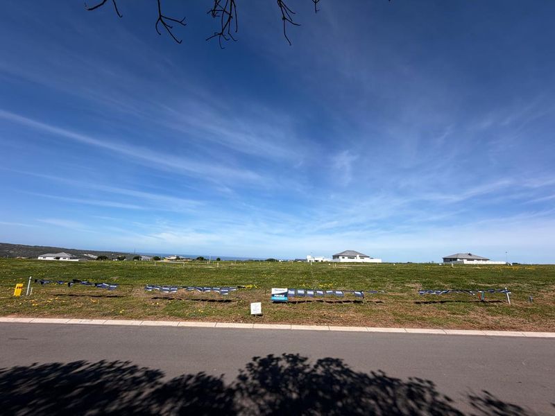 A vacant residential plot of land featuring a grassed surface, situated along a paved road with distant coastal views.