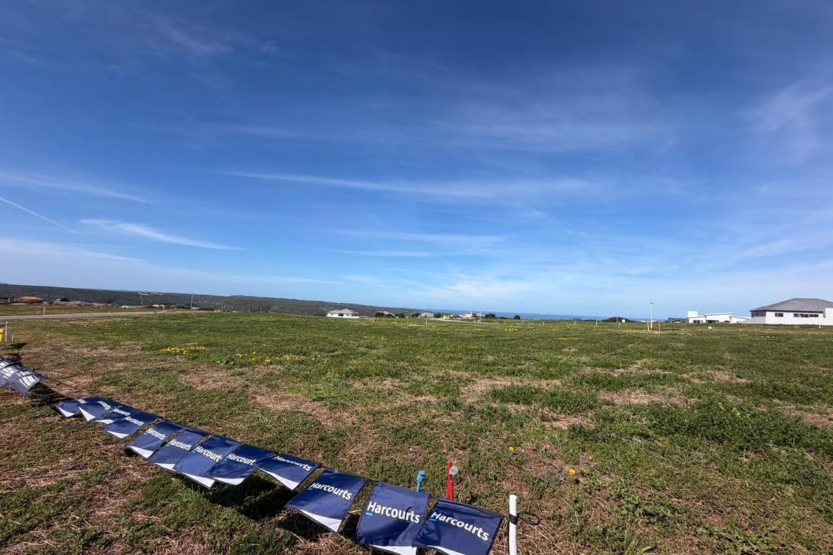 A wide-angle view of a vacant residential plot of land with surrounding neighborhood development visible in the distance.