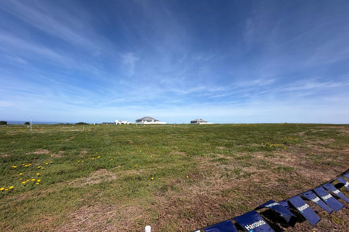 A wide-angle view of a large, flat vacant residential plot with surrounding coastal landscape and distant neighboring properties.