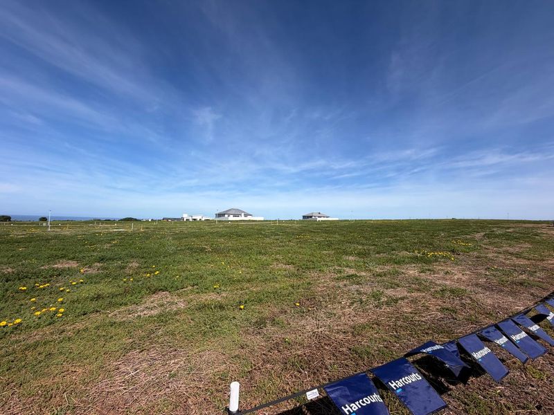 A wide-angle view of a large, flat vacant residential plot with surrounding coastal landscape and distant neighboring properties.