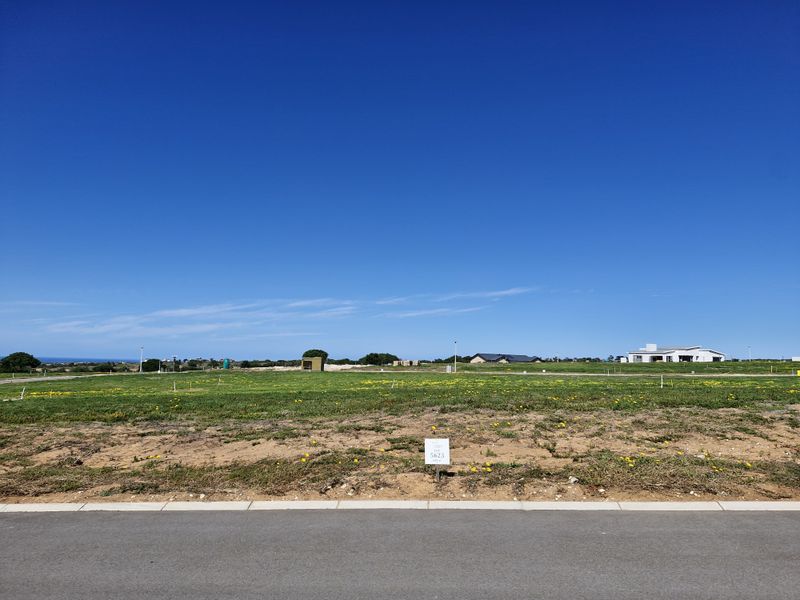 A vacant residential plot of land featuring a level grass surface, paved road access, and clear boundaries in a developing estate.