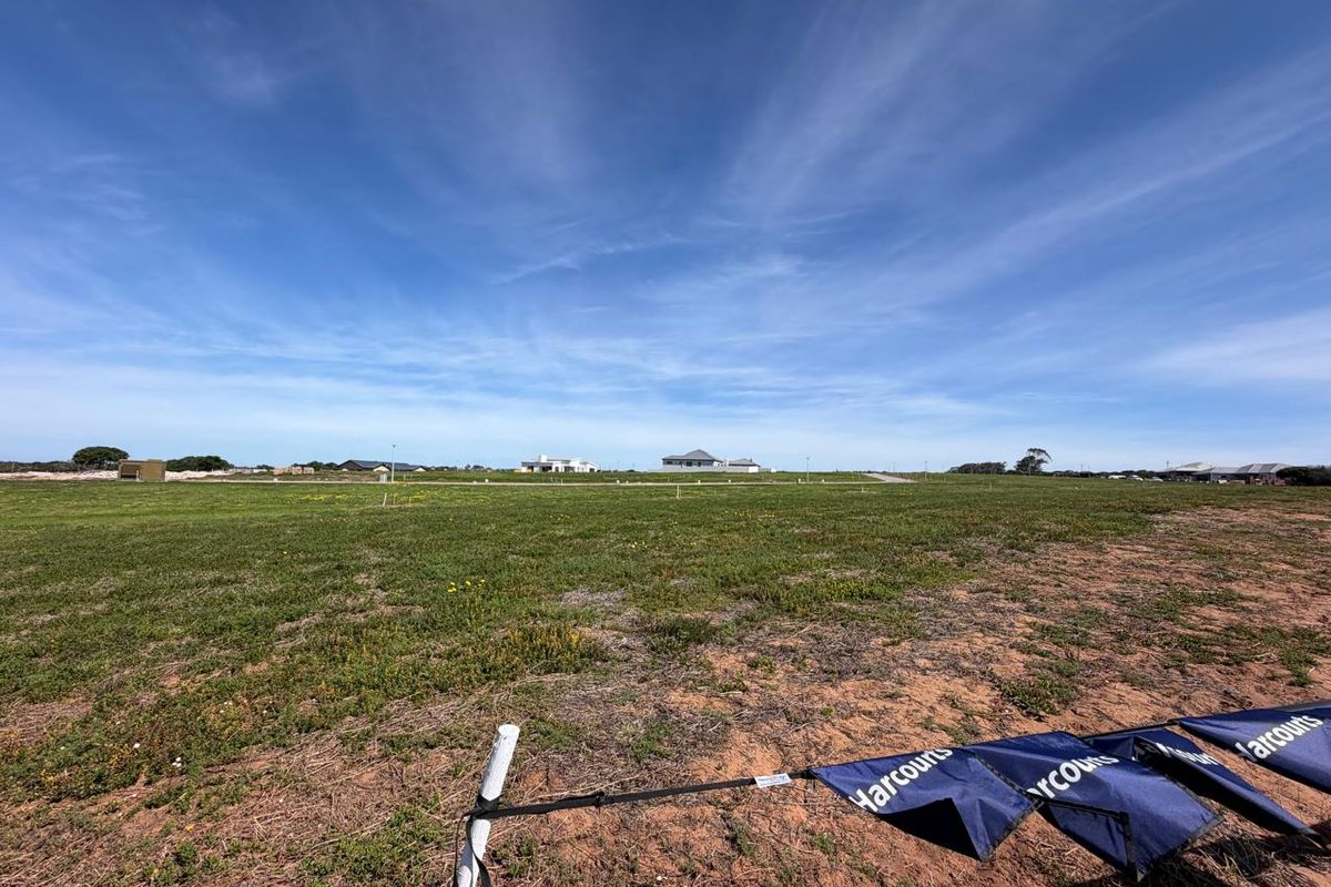 A wide-angle view of a vacant residential plot of land with surrounding neighborhood development visible in the distance.