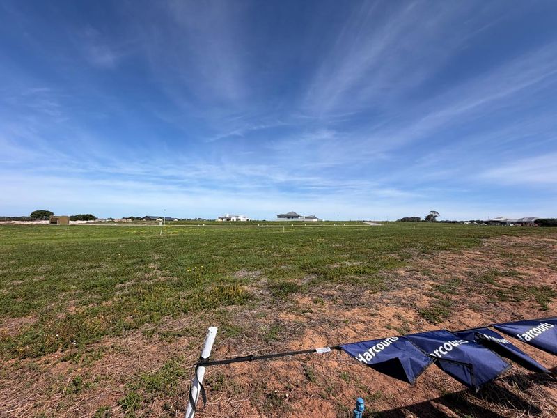 A wide-angle view of a vacant residential plot of land with surrounding neighborhood development visible in the distance.