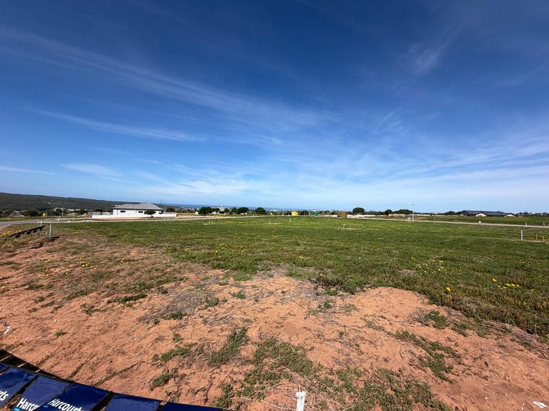 A wide-angle view of a vacant residential plot featuring natural ground cover and clear boundary markers in a developing neighborhood.