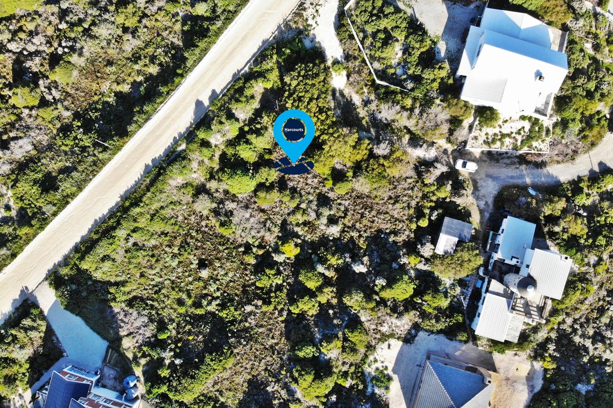 An aerial view of a vacant residential plot featuring natural vegetation, situated in a developed coastal or rural neighborhood.