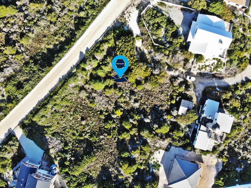 An aerial view of a vacant residential plot featuring natural vegetation, situated in a developed coastal or rural neighborhood.