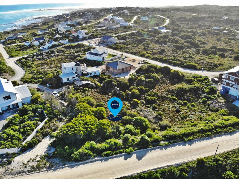 Aerial view of a vacant residential plot situated in a coastal estate, surrounded by established homes and natural vegetation.