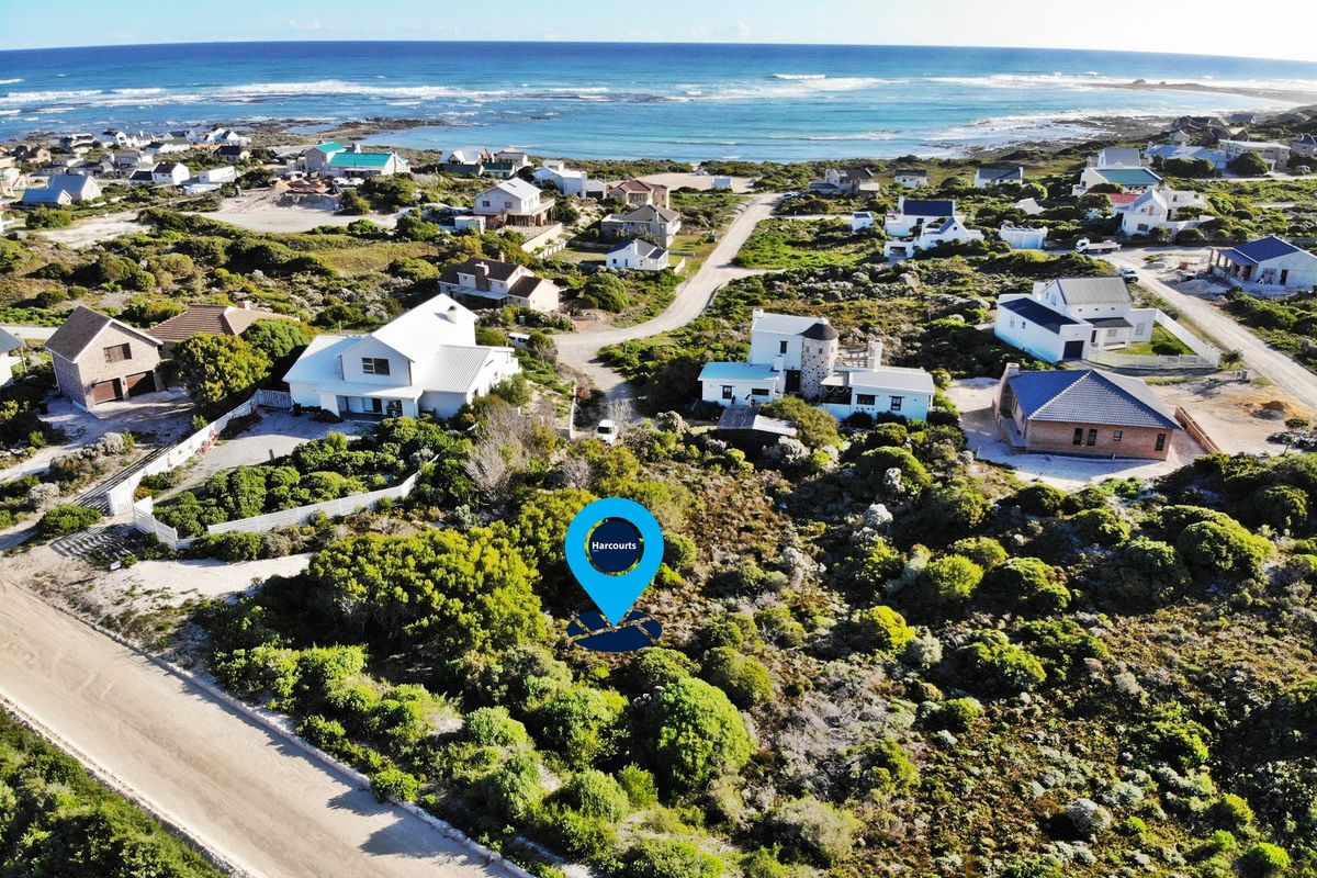 An aerial view of a vacant residential plot situated in a coastal neighborhood, featuring natural vegetation and proximity to the ocean.