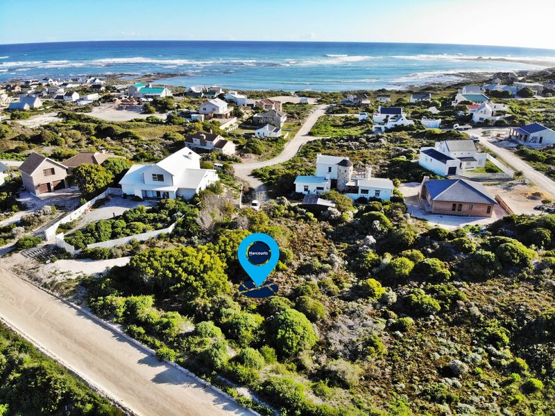 An aerial view of a vacant residential plot situated in a coastal neighborhood, featuring natural vegetation and proximity to the ocean.