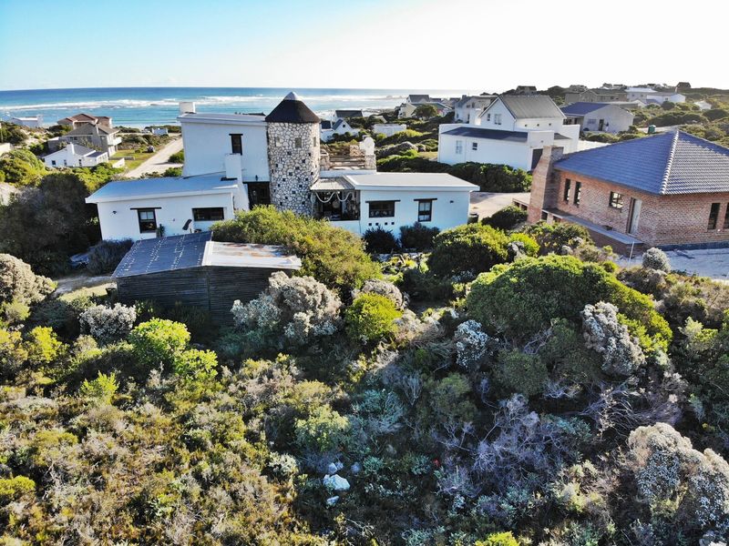 Aerial view of a coastal residential property featuring a unique stone turret design, surrounding native vegetation, and proximity to the ocean.