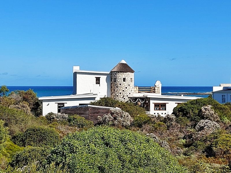 A scenic view of a coastal property featuring unique stone architecture and a thatched roof, set against a backdrop of the ocean.