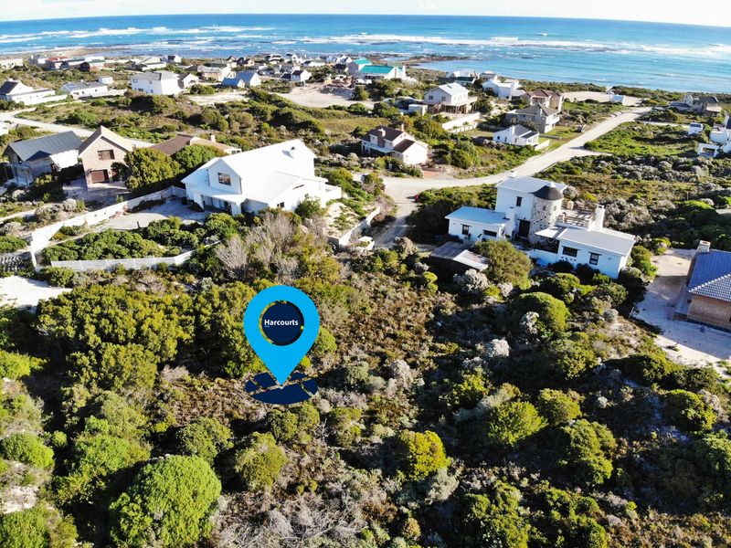 Aerial view of a vacant residential plot situated in a coastal neighborhood, surrounded by established homes and natural vegetation.