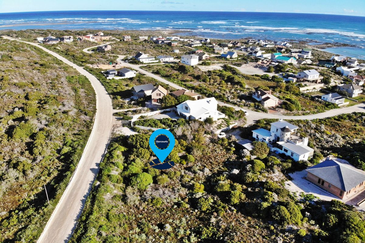 Aerial view of a vacant residential plot situated in a coastal neighborhood with surrounding vegetation and proximity to the ocean.