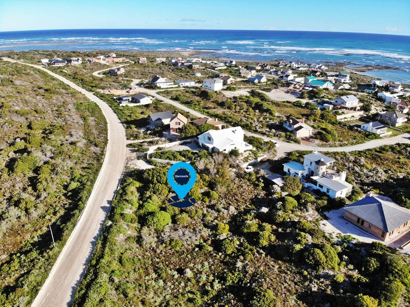 Aerial view of a vacant residential plot situated in a coastal neighborhood with surrounding vegetation and proximity to the ocean.