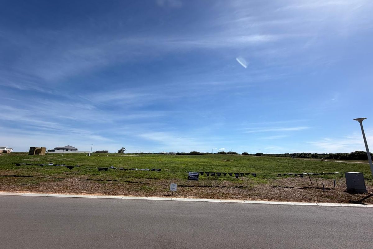 A vacant residential plot of land featuring a level grass surface, accessible from a paved road with existing utility infrastructure.