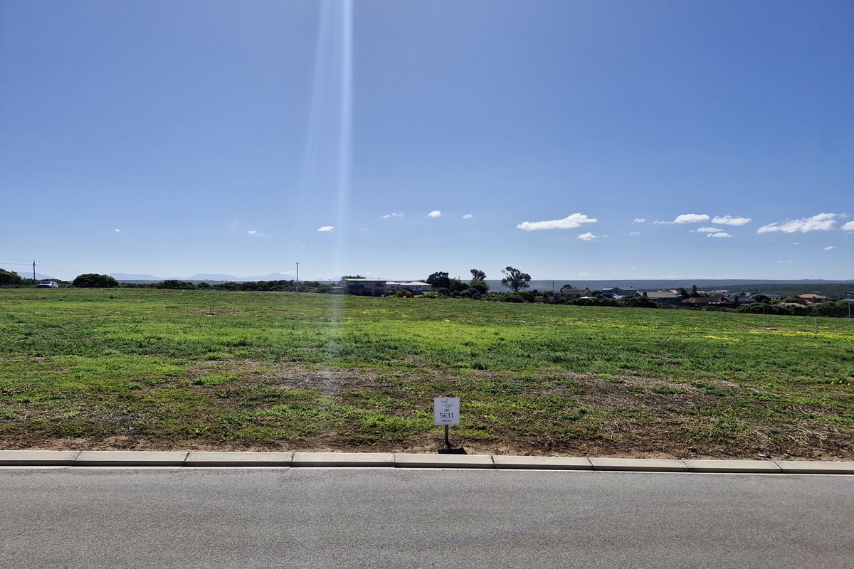 A vacant residential plot of land viewed from the street, featuring open grass terrain and a clear view of the surrounding neighborhood.