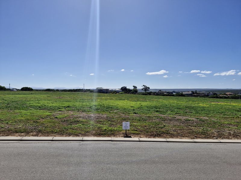 A vacant residential plot of land viewed from the street, featuring open grass terrain and a clear view of the surrounding neighborhood.