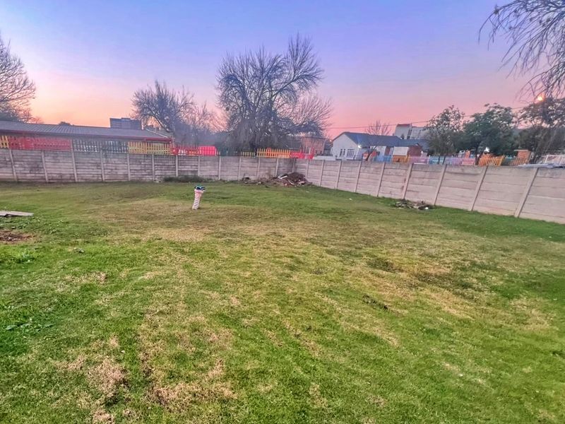 A spacious backyard area featuring a grass lawn enclosed by a precast concrete boundary wall.