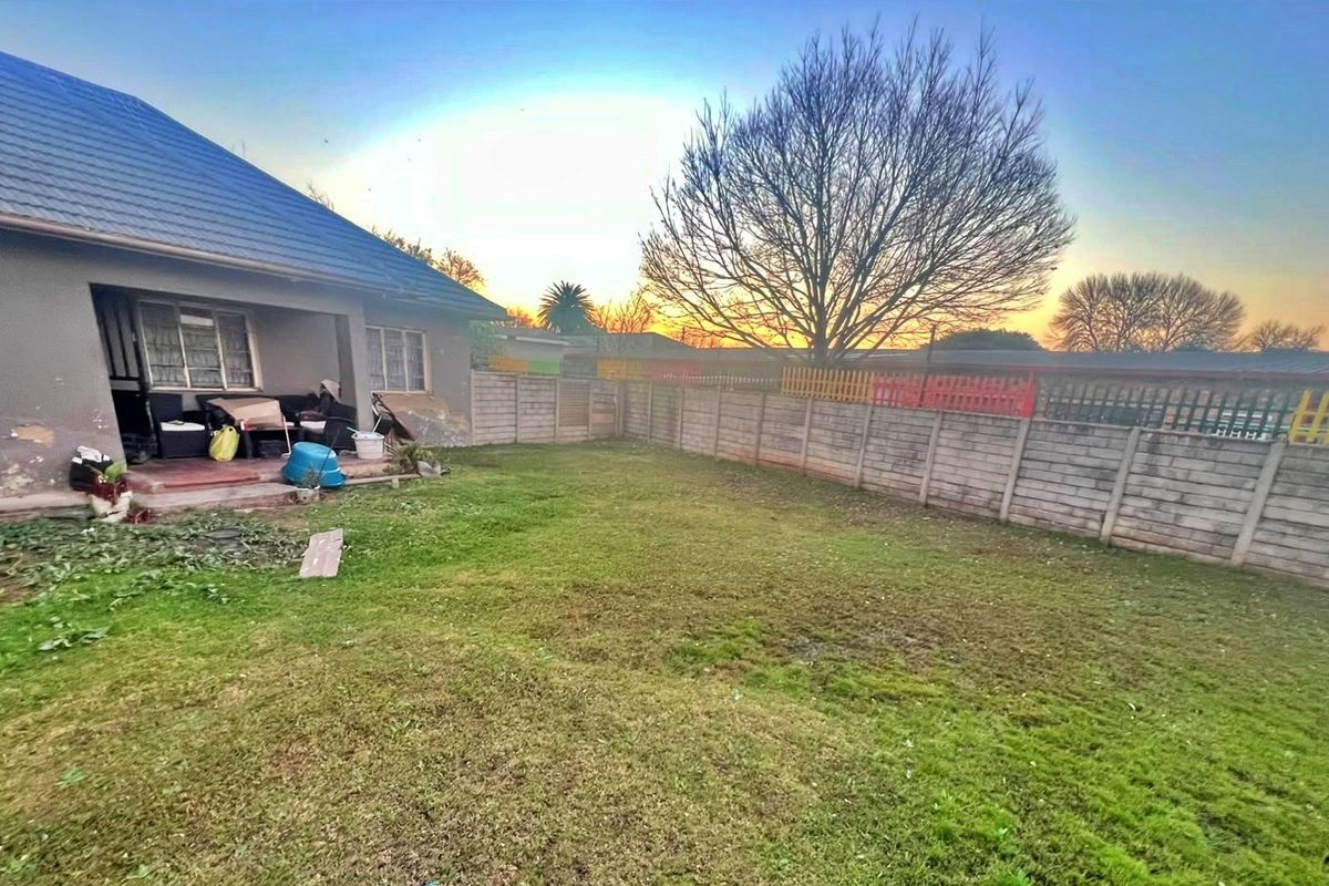 Rear view of the property featuring a lawn, precast concrete boundary wall, and a covered patio area with visible exterior wall maintenance required.