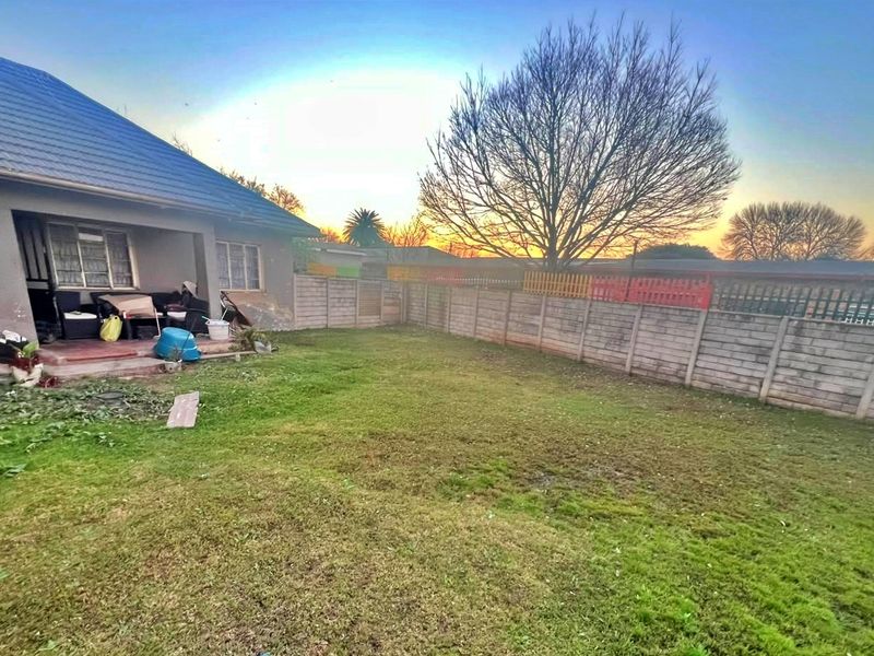 Rear view of the property featuring a lawn, precast concrete boundary wall, and a covered patio area with visible exterior wall maintenance required.